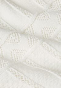 Biały dzianinowy materiał z wzorem rombów z ażurowymi detalami. Miękka tekstura i równe szwy tworzą jednolity wygląd.