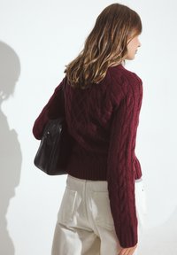 Bordo adīto džemperis ar ribotu apakšu un garām piedurknēm, kombinēts ar krēmkrāsas biksēm un melnu plecu somu.