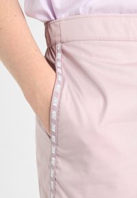 Helle rosa Shorts mit einer glatten Textur, ausgestattet mit einer Seitentasche und einem kontrastierenden weißen Nike-Logo am Bund.