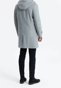 Abrigo gris con capucha hecho de tela texturizada, con corte recto y costuras laterales. Combinado con pantalones de cuadros negros y botines hasta el tobillo.