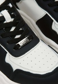 Czarno-białe trampki z gładką skórzaną cholewką, perforowanym noskiem i czarnymi sznurowadłami. Srebrny akcent logo na języku.