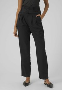 Pantalons noirs taille haute avec une jambe large, dotés d'une ceinture avec une boucle rectangulaire, de plis et de poches latérales. Texture de tissu lisse.