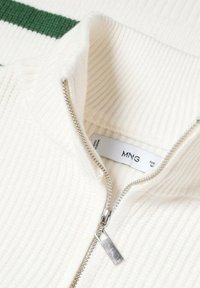 Sweater blanc côtelé zippé avec un col montant. Fermeture éclair argentée avec un tirant. L'étiquette intérieure indique "MNG." Le fond présente des rayures vertes.