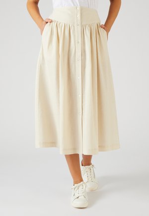 Beige, gerippter Midirock mit hoher Taille, vorne mit Knopfverschluss und Taschen. Kombiniert mit weißen Sneakern.