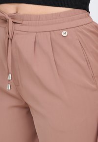 Helle rosa Jogginghosen mit einem elastischen Bund, Kordelzug und silbernen Hardware-Akzenten. Besitzt Falten und ein Metallschriftzug-Detail.