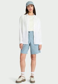 Lightweight white linen shirt over a light-colored t-shirt, paired with blue shorts. Accessorized with a light blue cap and beige shoes.