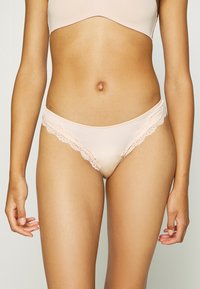 Lichtroze satijnen thong met kant langs de randen, voorzien van een gladde textuur en een lage taille. Geen extra patronen of hardware.