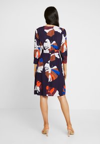 Ein dunkelblaues Kleid mit floralen Mustern in Rot, Orange und Weiß, das lange Ärmel, eine taillierte Taille und einen knielangen Saum hat.