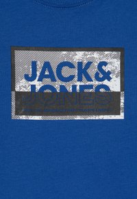 Zils kokvilnas T-krekls ar melnbaltu grafisko apdruku, kurā ir teksts "JACK & JONES", horizontālas līnijas un koordinātas apakšā.