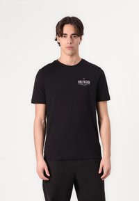Zwarte T-shirt met korte mouwen en een ronde halslijn, voorzien van een witte "HILFIGER" logo op de borst. Gemaakt van gladde katoen stof.