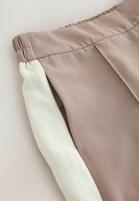 Gros plan d'un pantalon beige avec une taille élastique et une bande de tissu blanche contrastante le long de la couture latérale.