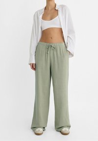 Loungebroek in een zachte groene stof, met een elastische tailleband en trekkoord, volwaardige lengte met een ontspannen pasvorm, gecombineerd met een witte top.