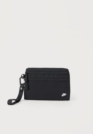 Bolsa rectangular negra de Nike con dos compartimentos con cremallera y una correa de muñeca desmontable sobre fondo claro.