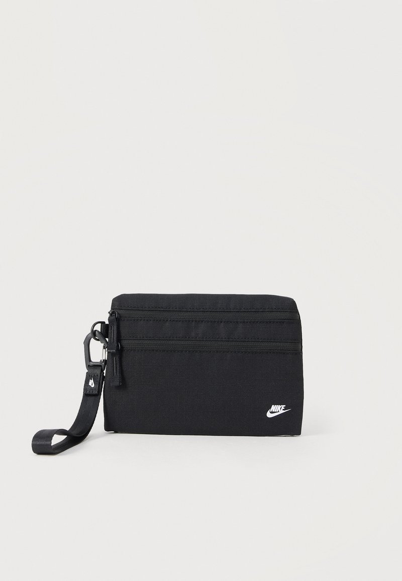 Bolsa rectangular negra de Nike con dos compartimentos con cremallera y una correa de muñeca desmontable sobre fondo claro.