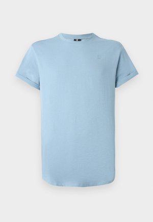Camiseta de cuello redondo de manga corta en azul claro con un pequeño logo tono sobre tono en el lado izquierdo del pecho y puños de manga ligeramente enrollados.