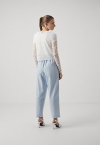 White lace cropped top with long sleeves, paired with light blue high-waisted trousers and white and black heeled shoes.