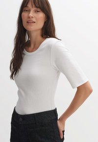 Top bianco a coste con maniche corte e scollatura rotonda, abbinato a pantaloni in denim scuro a vita alta con tasche e un dettaglio con bottone.