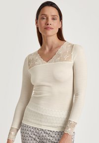 Romantische crèmekleurige top met lange mouwen en een geribbelde textuur, voorzien van een kanten V-hals en kanten accenten op de mouwen, gecombineerd met geblokte pantalons.