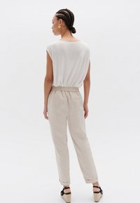 Lichtbeige linnen broek met een elastische tailleband en omgeslagen zomen, gecombineerd met een witte, losse top. De outfit is simpel en neutraal.
