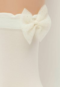 Bílé podkolenky s texturovaným lemem a pr�ůhlednou, třpytivou bílou mašlí na vršku, s jemným vzorem a měkkou tkaninou.