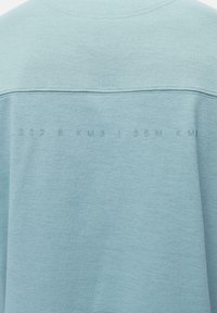 Šviesiai mėlyna džemperis, pasižymintis lygiu paviršiumi ir atspausdintu užrašu ant nugaros, kuriame yra skaitmenys ir raidės kontrastinga spalva.