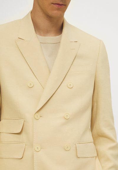 Beige dubbele-breasted blazer van zachte stof met vier knopen aan de voorkant, twee klepzakken en een piekrevers.