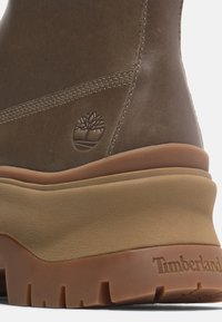 Talons de bottes en cuir marron avec logo d’arbre embossé et semelle épaisse en caoutchouc beige avec la marque Timberland sur la semelle extérieure crantée.