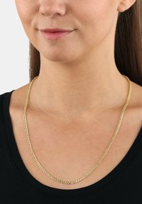 Collarín de cadena de oro con un diseño liso e entrelazado. La cadena se encuentra plana sobre la clavícula en una camisa oscura.