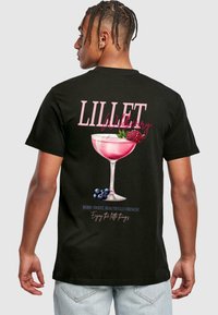 Sort T-shirt med et grafisk motiv af et pink cocktailglas med hindbær og blåbær, samt tekst der lyder "LILLET Wildberry."