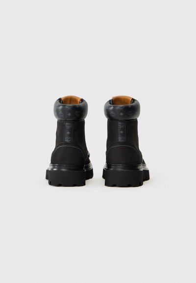 Bottines noires avec un poignet en cuir texturé, des coutures contrastées et une semelle en caoutchouc robuste, présentant un branding discret sur le poignet.