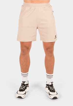 Shorts de sport beige avec une surface texturée, une taille élastique et des poches latérales. Accents de logo noir sur la jambe gauche.