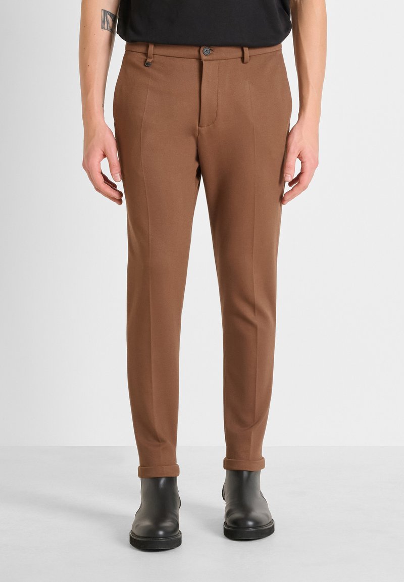 Pantalons marron effilés en tissu lisse, avec une fermeture à bouton, des poches latérales et des revers, associés à des bottes noires.
