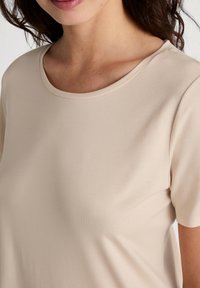 Camicetta beige a maniche corte con scollatura rotonda, tessuto liscio e leggero, caratterizzata da cuciture minime e un design semplice.