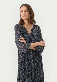 Rochie lungă bleumarin cu flori, cu mâneci 3/4, decolteu în V și material ușor. Prezintă modele complexe de flori în culori deschise.