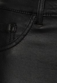 Tecido de denim preto em close, apresentando uma textura suave, costuras proeminentes e um acabamento ligeiramente brilhante. Inclui um pequeno detalhe de bolso.