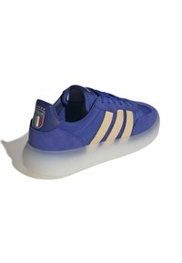 Modré semišové tenisky s třemi hnědými pruhy, průhlednou podrážkou a nášivkou s Itálií na patě. Kulatá špička a šněrovací design.