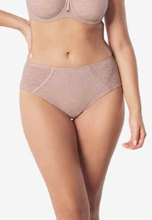 Kobieta ubrana w cielisty koronkowy biustonosz i dopasowane wysokie majtki, stojąca z jedną ręką na biodrze na neutralnym tle.