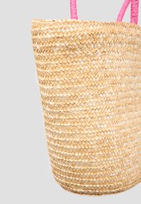 Kudottu oljettu laukku sylinterimäisellä muotoilulla, jossa on vaaleanpunaiset köysikahvat ja luonnollinen beige väri. Sileä pinta ja tasainen kuvio.