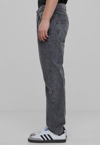 Jeans din denim gri cu o croială dreaptă, având un design clasic cu cinci buzunare și o textură ușor decolorată. Asortați cu adidași albaștri și negri.