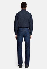 Jeans in denim scuro con una vestibilità dritta, abbinati a una camicia button-up scura. Il tessuto ha una consistenza liscia e un leggero lucido.