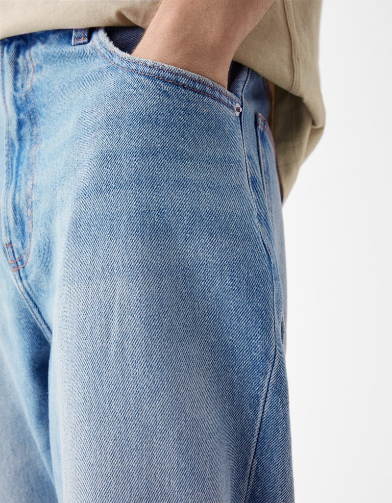 Nahaufnahme einer Person, die hellblaue Jeans trägt und ihre rechte Hand in der Vordertasche hat, vor einem schlichten weißen Hintergrund.