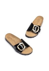 Sandales à glissière en vernis noir avec une large sangle et une grande boucle dorée, dotées d'un coussin de pied beige et d'une semelle en caoutchouc texturé.