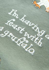 Olive green fabric with white embroidered text: "I'm having a feast with a gruffalo." Features a playful design with graphic accents.