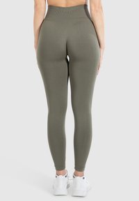 Leggings verde oliva a vita alta realizzati in materiale elasticizzato, con una texture liscia e un design aderente. Indossati con scarpe da ginnastica bianche.