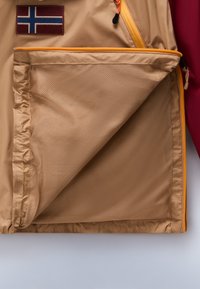 Beige yderstof med en mesh-lomme. Har orange lynlås og detaljer. Islandske flag-patch på venstre side. Glat tekstur.