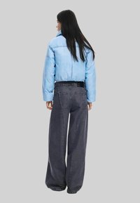 Hele sinine lühike jakk, millel on lai krae, on kombineeritud kõrge vöökohaga tumedate hallide laiadest teksapükstest, millel on tagataskud ja tekstuuritud viimistlus.