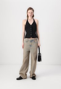 Top nero a halter con bottoni, dalla silhouette aderente, abbinato a jeans beige larghi e scarpe nere. Borsa scura in mano.