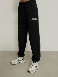 Juodos sportinės kelnės iš minkštos medžiagos su elastinga juosta. Ant šono išsiuvinėtas baltoje spalvoje „LAMANIA“ logotipas. Derinama su baltais sportbačiais.