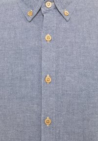 Camisa de botón azul claro con un patrón de espiga, que cuenta con siete botones color topo y un cuello clásico. Tejido texturizado con un brillo sutil.