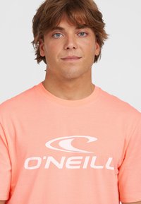 Camiseta de manga corta color rosa claro, hecha de algodón, con un gran logo blanco "O'Neill" en el pecho y un diseño de cuello redondo.